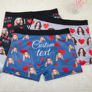 May include: Three pairs of boxer briefs with custom photo prints. One pair is black with "I ❤️ MY WIFE" text and red hearts. Another is blue with custom text and faces. The third is gray with red hearts.