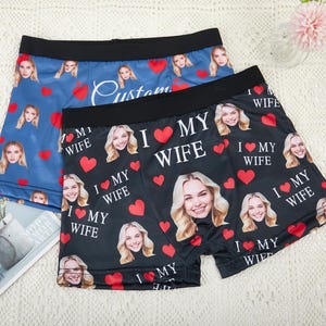 May include: Two pairs of boxer briefs. One pair is blue with a pattern of faces and red hearts, with the word "Custom" in white script. The other pair is black with faces, red hearts, and the text "I MY WIFE".