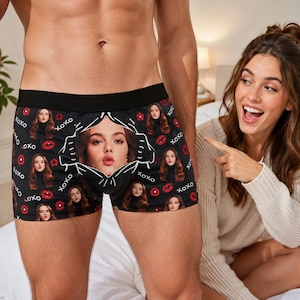 Puede incluir: Calzoncillos tipo bóxer negros con un patrón repetitivo del rostro de una mujer, labios rojos y el texto XOXO. El centro de la prenda muestra un retrato más grande y único del mismo rostro femenino enmarcado por un contorno gráfico blanco.