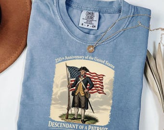 May include: A light blue t-shirt featuring a graphic commemorating the 250th anniversary of the United States. The graphic depicts a patriot holding a flag and rifle, with the text "DESCENDANT OF A PATRIOT". The shirt has a Comfort Colors tag.