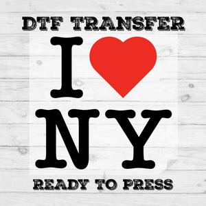 May include: DTF transfer with the text "I ❤️ NY" in black letters and a red heart. The words "READY TO PRESS" are below the text. The design is on a white background with a wood grain pattern.