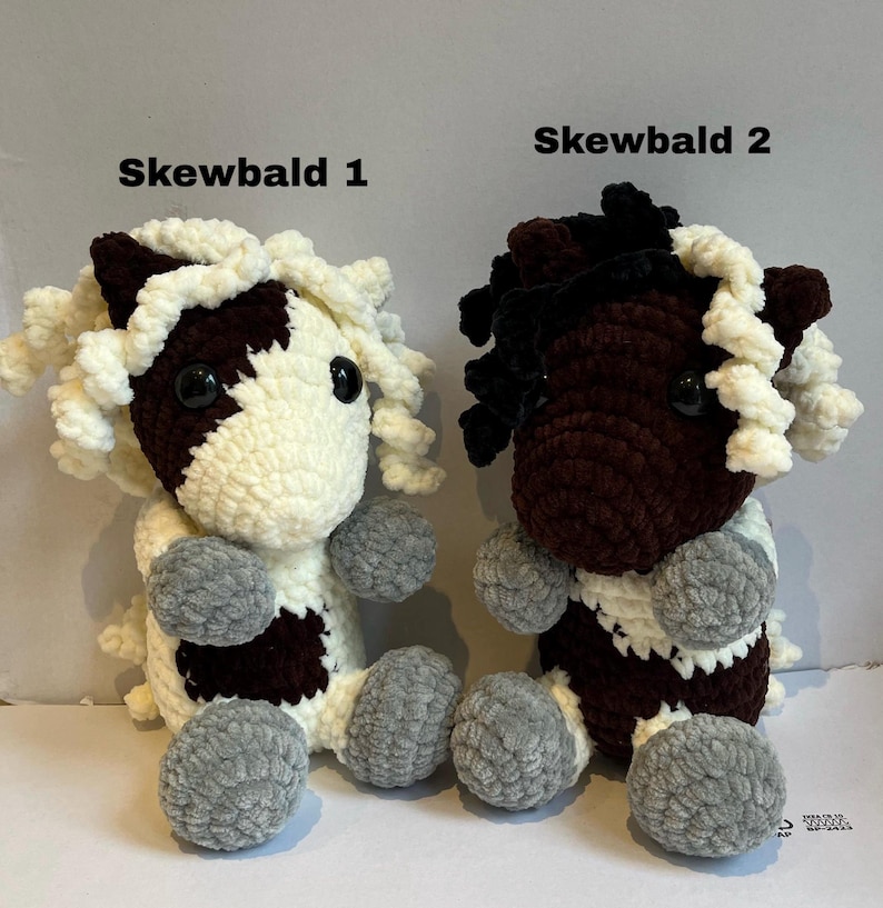 May include: Two handmade crochet horse plushies. One is white and brown with gray hooves, the other is brown and black with gray hooves. Both have curly white manes and the text "Skewbald 1" and "Skewbald 2" above them.