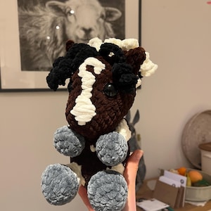 May include: A handmade crochet horse plushie in brown, white, and black. The horse has a white blaze, black mane and tail, and gray pom-pom feet. The plushie is a soft, cuddly toy.