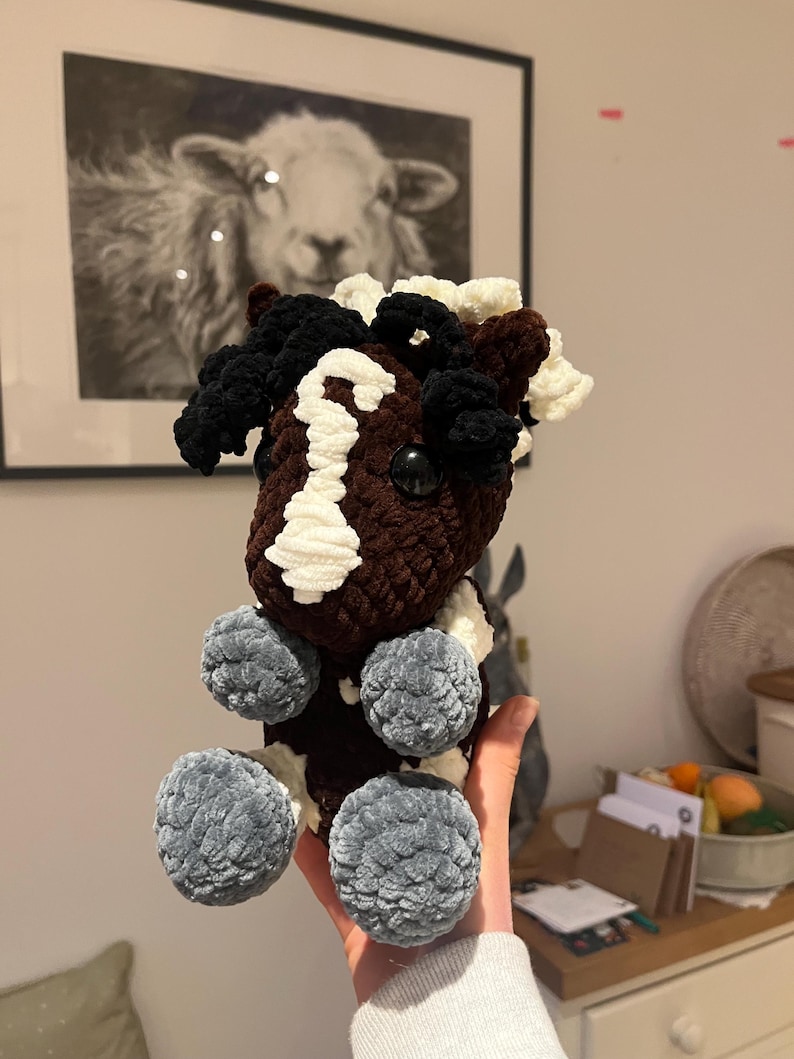 May include: A handmade crochet horse plushie in brown, white, and black. The horse has a white blaze, black mane and tail, and gray pom-pom feet. The plushie is a soft, cuddly toy.