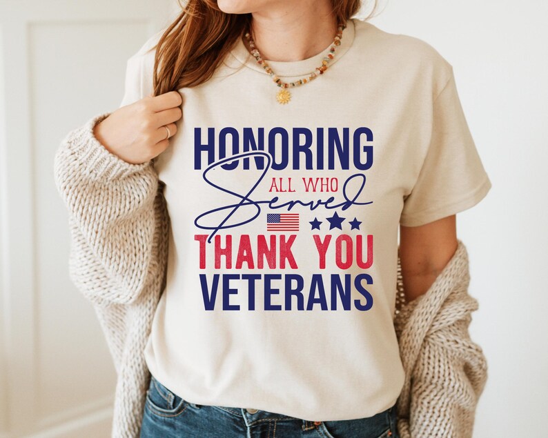 May include: A white t-shirt with a blue and red graphic that says "Honoring All Who Served Thank You Veterans". The graphic includes a small American flag and stars.