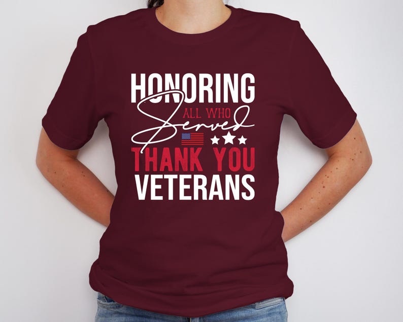 May include: A maroon t-shirt with white text that reads "Honoring All Who Served Thank You Veterans". The text is in a cursive font with a small American flag graphic above the word "Thank".