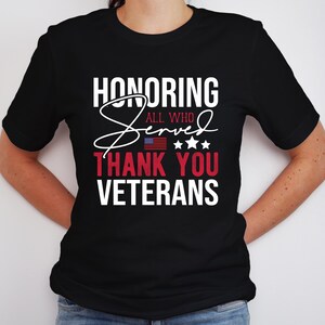 May include: Black t-shirt with white text that reads "Honoring All Who Served Thank You Veterans". The text is in a stylized font with a red, white, and blue American flag graphic.