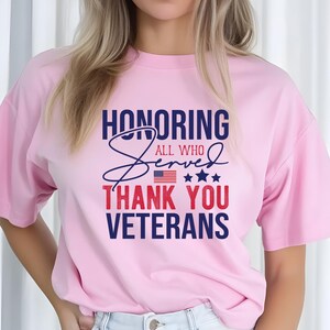 May include: Pink t-shirt with a blue and red graphic that says "Honoring All Who Served Thank You Veterans" with a small American flag and stars.
