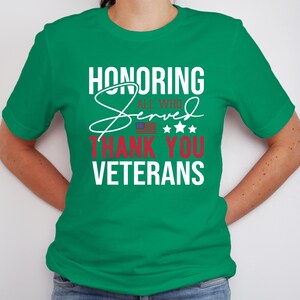 May include: A green t-shirt with the text "Honoring All Who Served Thank You Veterans" in white and red lettering. The text is stylized with a white cursive "Served" and a small American flag.