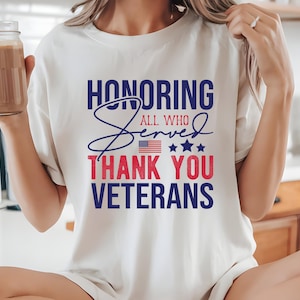 May include: White t-shirt with a blue and red graphic that says "Honoring All Who Served Thank You Veterans" with a small American flag and stars.