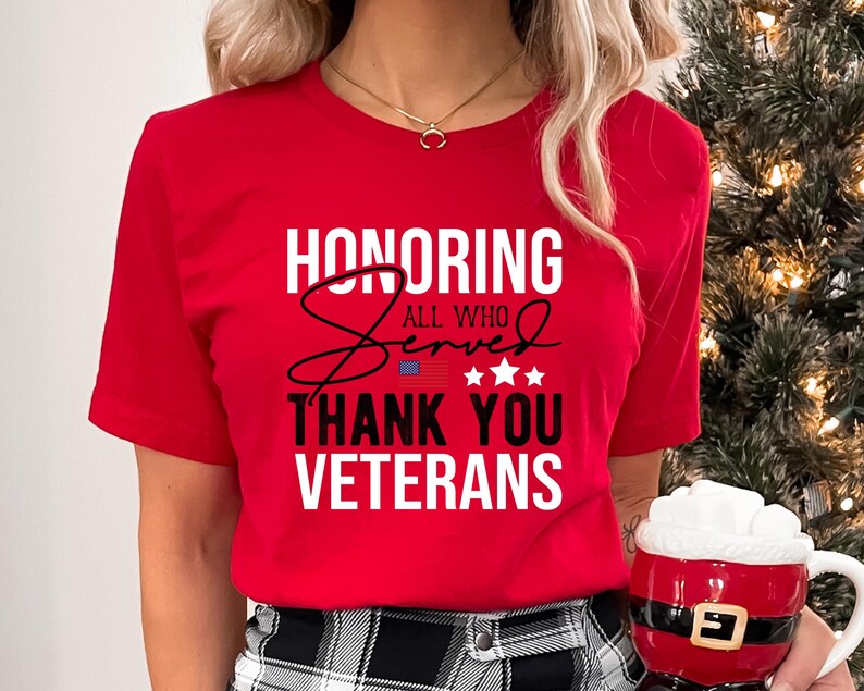May include: Red t-shirt with white text that reads "Honoring All Who Served Thank You Veterans". The text is in a bold, cursive font. There is a small American flag graphic and five stars above the word "Served".