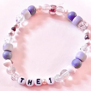 Handmade “The 1” friendship bracelet inspired by Taylor Swift’s Folklore album. Features white, grey, and silver beads with white howlite stone accents and “The 1” letter beads on elastic stretch cord. Created with a mix of glass, plastic, and whenever possible, upcycled and thrifted beads. Perfect for Swifties, Folklore fans, friendship bracelet collectors, concert outfits, bracelet stacks, and unique handmade gifts.