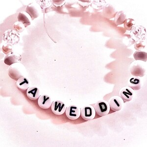 Handmade “taywedding” friendship bracelet inspired by Taylor Swift and Travis Kelce featuring white beads on elastic stretch cord with a romantic wedding-inspired aesthetic. Elegant pop culture inspired bracelet perfect for Swifties, friendship bracelet trading, concert outfits, bridal inspired jewelry, feminine bracelet stacks, and trendy handmade accessories.