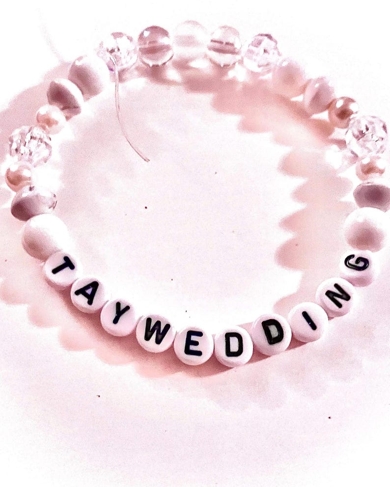 Handmade “taywedding” friendship bracelet inspired by Taylor Swift and Travis Kelce featuring white beads on elastic stretch cord with a romantic wedding-inspired aesthetic. Elegant pop culture inspired bracelet perfect for Swifties, friendship bracelet trading, concert outfits, bridal inspired jewelry, feminine bracelet stacks, and trendy handmade accessories.