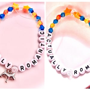 collage showcasing two handmade Taylor Swift The Life of a Showgirl inspired friendship bracelets. Both feature the phrase “Actually Romantic” in letter beads, celebrating the sweet and dreamy track from the album. One bracelet is designed in bold orange and green/teal beads, while the other is crafted in soft pink tones. Made with stretchy elastic, glass, and plastic beads, these Swiftie bracelets are perfect jewelry gifts, concert accessories, or collectible fan merch