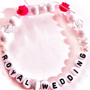 Handmade “royal wedding” friendship bracelet inspired by Taylor Swift and Travis Kelce featuring white and pink beads, elastic stretch cord, and two pink rose accents inspired by a romantic garden engagement aesthetic. Feminine pop culture inspired bracelet perfect for Swifties, concert outfits, friendship bracelet trading, romantic jewelry lovers, bracelet stacks, and trendy handmade accessories.