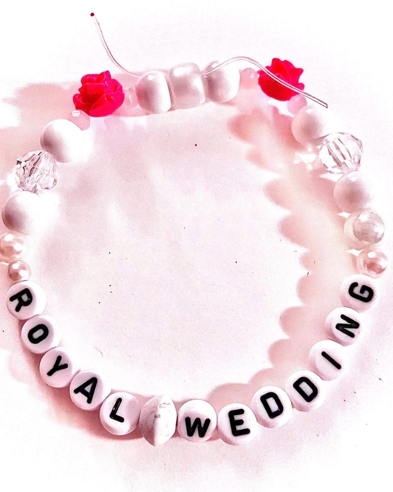 Handmade “royal wedding” friendship bracelet inspired by Taylor Swift and Travis Kelce featuring white and pink beads, elastic stretch cord, and two pink rose accents inspired by a romantic garden engagement aesthetic. Feminine pop culture inspired bracelet perfect for Swifties, concert outfits, friendship bracelet trading, romantic jewelry lovers, bracelet stacks, and trendy handmade accessories.