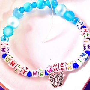 May include: A beaded bracelet featuring blue and light blue round beads, white square letter beads spelling out ONLY ME WHEN I M WITH U, and a silver-toned butterfly charm. The bracelet is strung on a clear elastic cord with varied bead sizes.