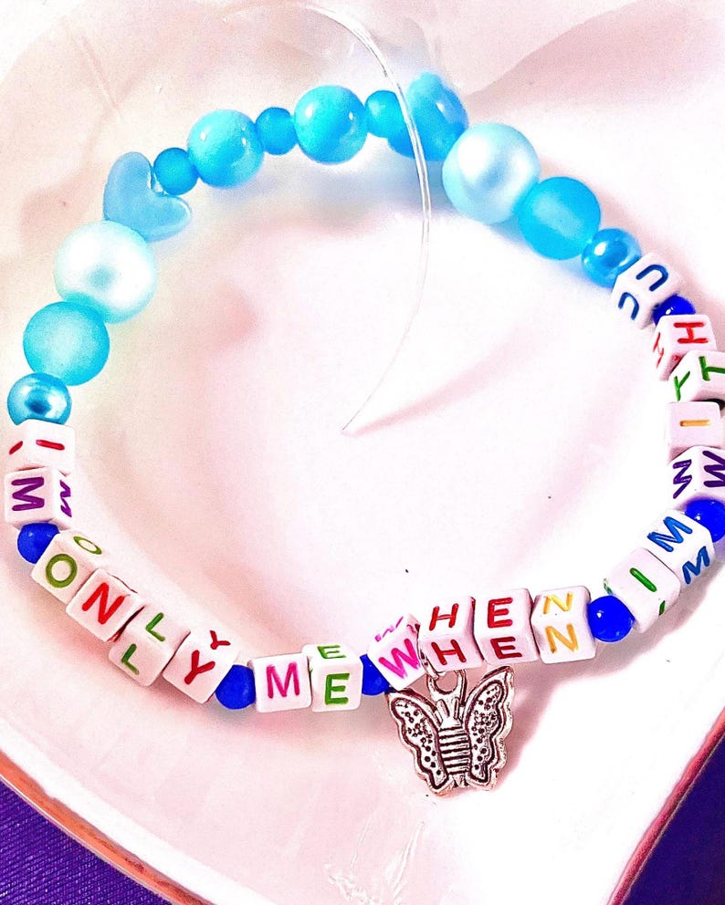 May include: A beaded bracelet featuring blue and light blue round beads, white square letter beads spelling out ONLY ME WHEN I M WITH U, and a silver-toned butterfly charm. The bracelet is strung on a clear elastic cord with varied bead sizes.