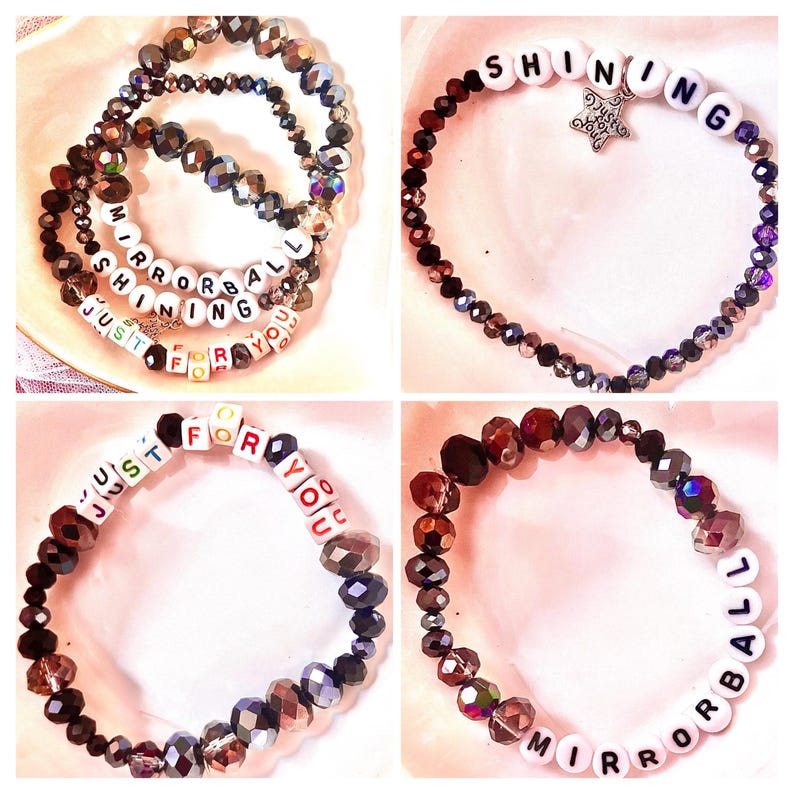 K&ouml;nnte beinhalten: Ein Set aus vier Perlenarmb&auml;ndern mit dunklen, facettierten, irisierenden Glasperlen und wei&szlig;en quadratischen Buchstabenperlen. Die Armb&auml;nder zeigen die Schriftz&uuml;ge "SHINING", "MIRRORBALL" und "JUST FOR YOU", eines enth&auml;lt einen sternf&ouml;rmigen Anh&auml;nger.