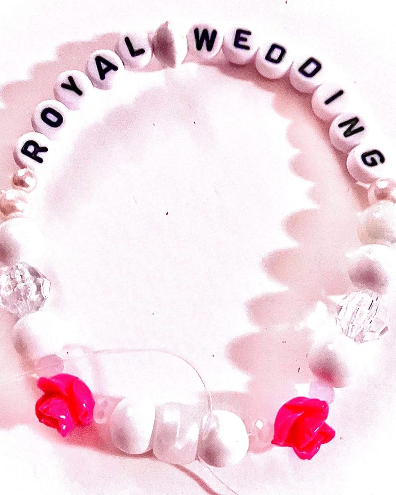 White and pink handmade “royal wedding” friendship bracelet inspired by Taylor Swift and Travis Kelce with soft romantic bead details and two pink rose accents. Elegant elastic stretch bracelet inspired by celebrity romance, garden engagement aesthetics, and American royalty style. Perfect for Swiftie collections, feminine bracelet stacks, concert accessories, friendship bracelet trading, and romantic pop culture jewelry.