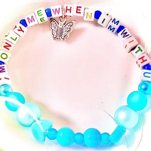 May include: A beaded bracelet featuring white square beads with colorful letters spelling out ONLY ME WHEN I'M WITH U, interspersed with blue beads. A silver-toned butterfly charm hangs from the top, and the bottom half consists of round light blue beads.