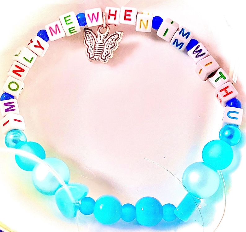 May include: A beaded bracelet featuring white square beads with colorful letters spelling out ONLY ME WHEN I'M WITH U, interspersed with blue beads. A silver-toned butterfly charm hangs from the top, and the bottom half consists of round light blue beads.