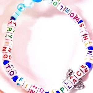 May include: A beaded bracelet featuring white square letter beads spelling out the phrase TRYING TO FIND A PLACE IN THIS WORLD in multicolored text. The bracelet includes blue round beads, a star-shaped bead, and a silver-toned metal charm.