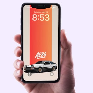 May include: A smartphone displays a wallpaper featuring a white and black car with gold rims, set against a gradient of orange and beige. The text "AE86" is above the car, with the date and time displayed at the top.