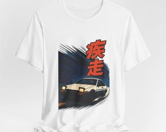 Può includere: Una t-shirt bianca con una stampa grafica di un'auto sportiva bianca con fari a scomparsa che derapa su una strada. Il design include linee di movimento blu scuro e grandi caratteri kanji rossi 疾走 sopra il veicolo.