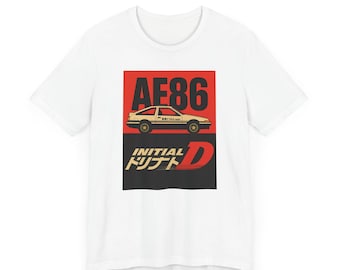 Può includere: Una t-shirt bianca a maniche corte con una stampa grafica di un'auto AE86 beige su sfondo rosso sopra il testo "INITIAL D" in lettere bianche e dorate, con caratteri giapponesi aggiuntivi stampati sotto l'auto e accanto alla lettera D.