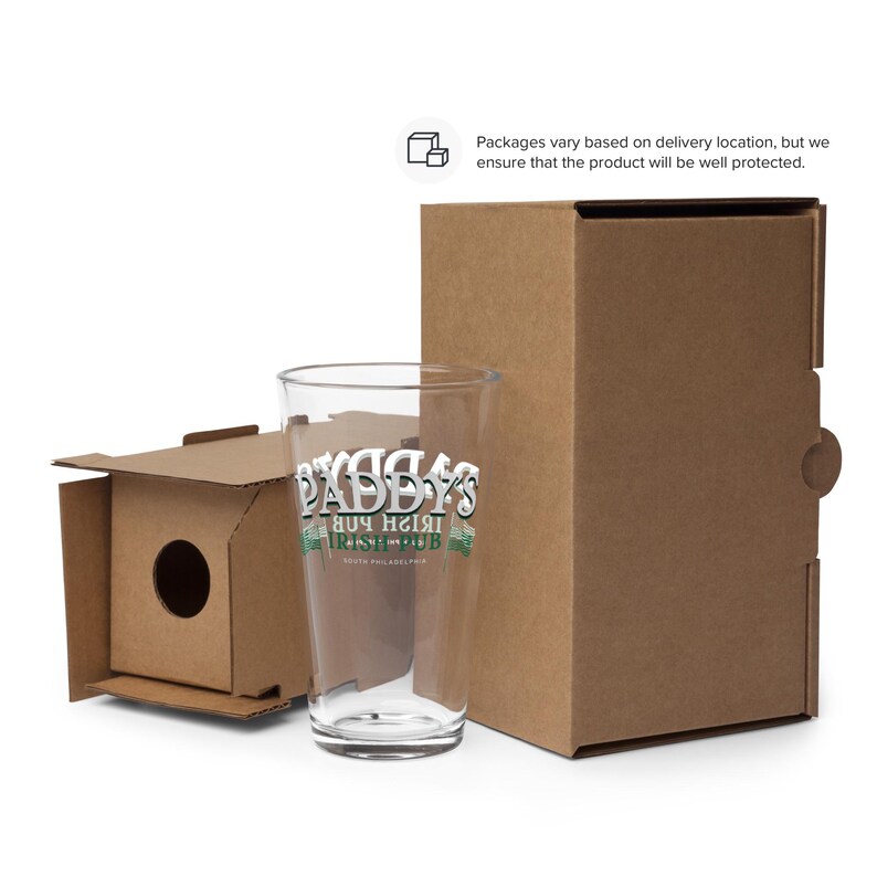 May include: A clear glass pint glass with a white and green graphic that says "Paddy's Irish Pub" on it. The glass is sitting on a brown cardboard box.