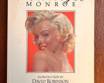 May include: A white book with the title "Marilyn Monroe" in black cursive lettering. The cover features a color photograph of Marilyn Monroe with a red background. The book includes the text "Introduction by David Robinson" and "Compiled and edited by John Kobal".