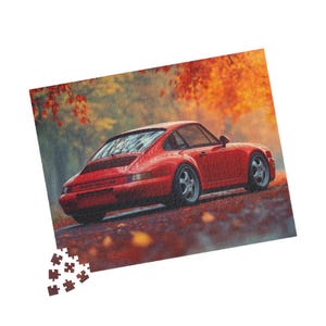 May include: A red Porsche 911 sports car parked in a forest setting with autumn leaves on the ground.