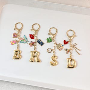 Pode incluir: Quatro porta-chaves de metal em tom dourado com as letras B, R, S e D. Cada porta-chaves inclui um fecho mosquetão e vários berloques coloridos, incluindo um coração rosa, borboleta, lábios vermelhos, lua e estrela, trevo, nuvem e um laço.