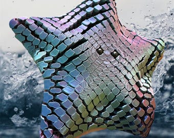 May include: A 3D printed iridescent blue and green star-shaped object with a textured surface. The object is floating in the air above a blue and white water surface.