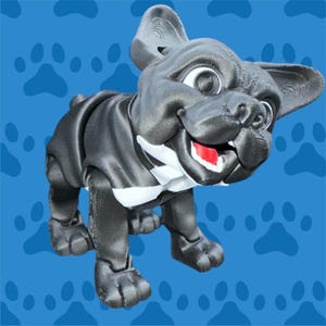 Puede incluir: Figura de bulldog francés en blanco y negro impresa en 3D. El perro tiene una expresión sonriente con una lengua roja, dientes blancos y ojos grandes y expresivos. Lleva un esmoquin blanco y negro. El fondo es azul con huellas de patas.