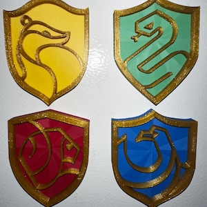 May include: Four Hogwarts house crests, each with a different animal and color. The crests are made of a 3D printed material with a gold glitter finish. The crests are for Gryffindor, Hufflepuff, Slytherin, and Ravenclaw.