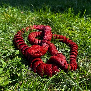 Puede incluir: Una escultura de serpiente roja enroscada hecha de madera. La escultura está sobre un lecho de hierba verde.
