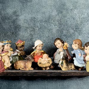 May include: A ceramic nativity scene featuring figures of the Holy Family, the Three Wise Men, and animals. The figures are painted in various colors and are arranged on a wooden shelf. The background is a textured gray.