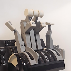 May include: A detailed model of an aircraft throttle quadrant, featuring multiple levers and controls. The model is primarily grey and black, with white accents and labels like "SPEED BRAKE" and "GO AROUND".