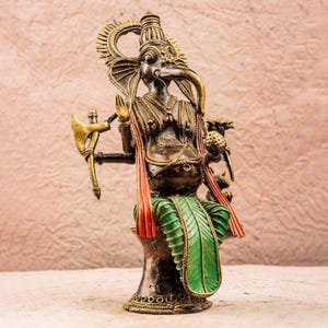 May include: A gold, green, and red metal statue of the Hindu deity Ganesha. The statue depicts Ganesha sitting on a throne with an axe in one hand and a sweet in the other.