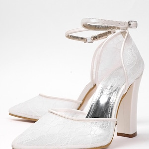 May include: A pair of white lace heels with a pointed toe and a thick, block heel. The shoes have an ankle strap with a silver buckle. The heels are approximately 3 inches (7.6 cm) high.