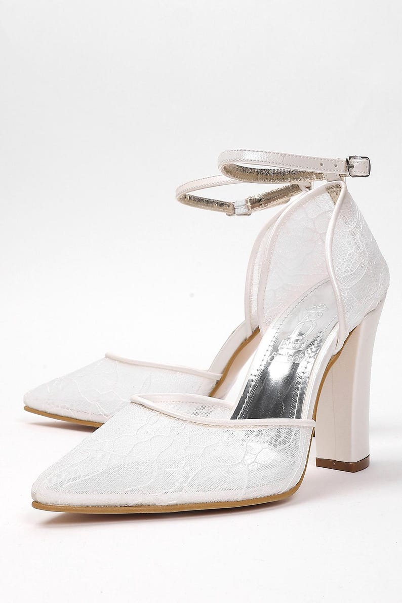 May include: A pair of white lace heels with a pointed toe and a thick, block heel. The shoes have an ankle strap with a silver buckle. The heels are approximately 3 inches (7.6 cm) high.