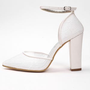 May include: White lace high-heeled shoe with a pointed toe and ankle strap. The heel is a thick, block style. The shoe features a delicate lace pattern and a small buckle on the ankle strap. The heel height is approximately 3.5 inches.