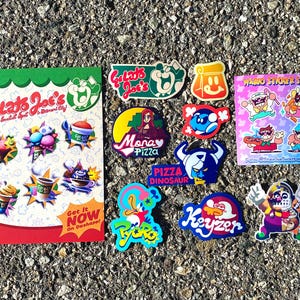 Op de afbeelding: Een verzameling kleurrijke stickers en een promotieflyer met de branding van Gelato Joe's. De flyer toont diverse illustraties van ijs en desserts met de tekst Gelato Joe's, The Essential Spot in Diamond City en Get It NOW On Dashapp.