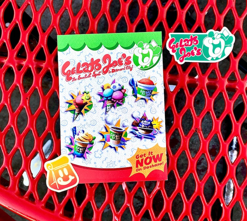 Op de afbeelding: Een rechthoekige flyer voor Gelato Joe's met kleurrijke illustraties van ijs, slushies en koffiedrankjes. De tekst luidt Gelato Joe's The Sweetest Spot in Diamond City! en Get It NOW On Dashapp! Twee extra stickers zijn inbegrepen.