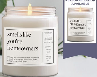Może przedstawiać: Biała świeca w przezroczystym szklanym słoiku z etykietą, na której widnieje napis "smells like you're homeowners". Świeca jest zapalona i płomień jest widoczny. Etykieta zawiera również tekst "Infused with the scent of new beginnings, a touch of mortgage paperwork, and a hint of home sweet home."