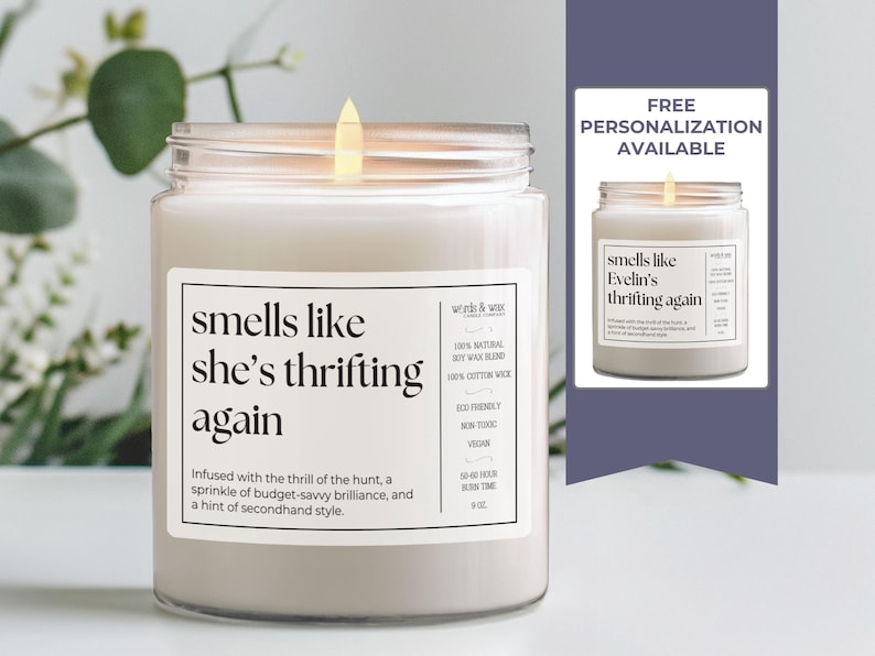 May include: A white candle with a clear glass jar and a black label that reads "smells like she's thrifting again". The label also includes the text "Infused with the thrill of the hunt, a sprinkle of budget-savvy brilliance, and a hint of secondhand style."