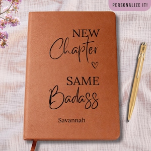May include: A brown leather-bound journal with the words "NEW Chapter SAME Badass" in black script. The name "Savannah" is printed at the bottom. A gold pen rests on the right side of the journal. The top right corner reads "PERSONALIZE IT!"